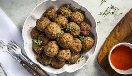A bowl containing lean beef meatballs with a sauce on the side, illustrating the concept of precautions for beef consumption.