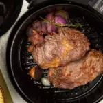 A piece of beef inside an air fryer being grilled along with onions and seasonings.