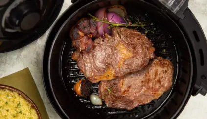 A piece of beef inside an air fryer being grilled along with onions and seasonings.