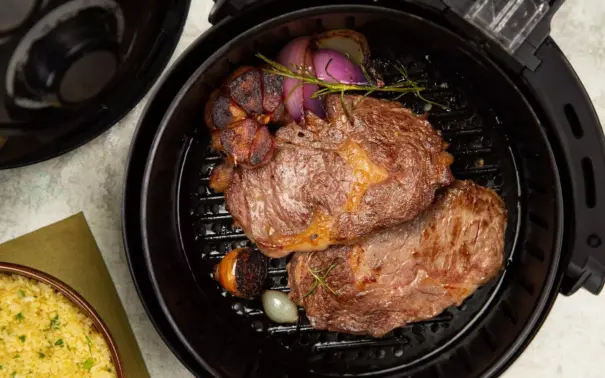 A piece of beef inside an air fryer being grilled along with onions and seasonings.