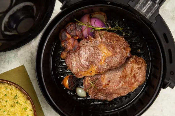 A piece of beef inside an air fryer being grilled along with onions and seasonings.