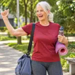 Smiling elderly woman in a park, stretching on a yoga mat and holding a water bottle, as part of a healthy aging nutrition concept