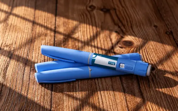 Two blue weight-loss pens, labeled for a 1 mg dose, resting on a wooden surface.