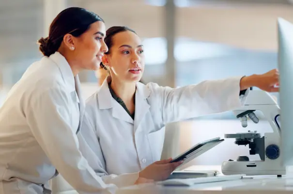 Dos científicas analizando resultados de investigación sobre prebióticos y probióticos en un laboratorio de microbiología veterinaria, con enfoque en la nutrición animal.
