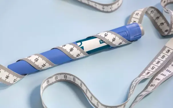 Pluma adelgazante azul con cinta métrica alrededor, instrumento popular para ayudar en la pérdida de peso y el control de las medidas corporales.