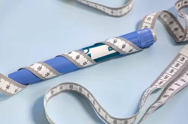 Pluma adelgazante azul con cinta métrica alrededor, instrumento popular para ayudar en la pérdida de peso y el control de las medidas corporales.