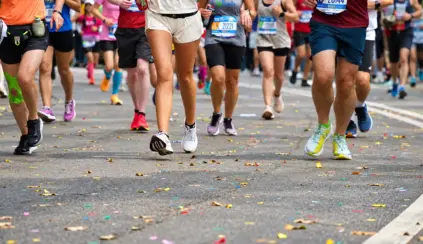 Un grupo de corredores, con números de inscripción bien visibles, corre por una calle cubierta de confeti de colores durante una carrera urbana o un maratón. Solo se ven sus piernas y pies, lo que demuestra la dedicación y la energía impulsadas por la proteína para corredores.