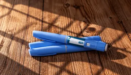 Dos plumas adelgazantes azules con la indicación de 1 mg, apoyadas sobre una superficie de madera.