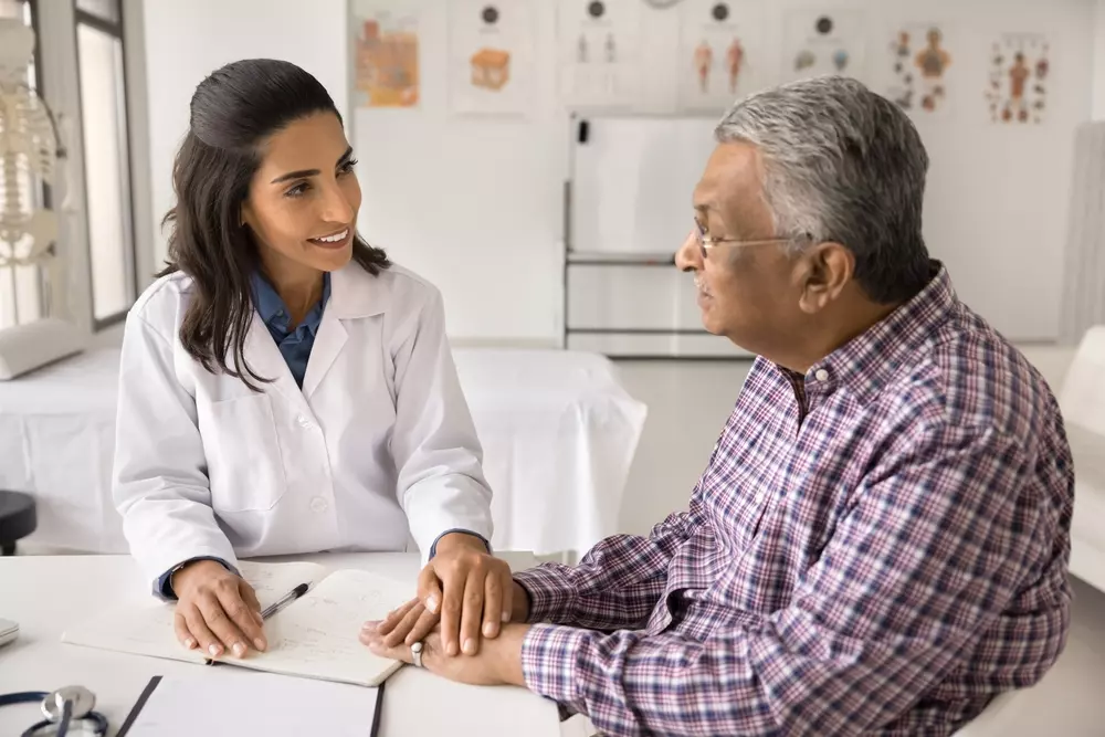 Um senhor idoso conversando com uma médica de aproximadamente 30/40 anos sobre sua saúde.