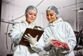 Duas pessoas em uniforme de proteção inspecionando armazenamento de carne em ambiente industrial