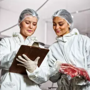 Duas pessoas em uniforme de proteção inspecionando armazenamento de carne em ambiente industrial