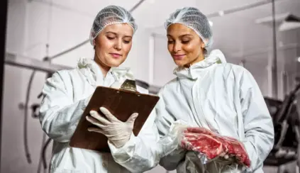 Duas pessoas em uniforme de proteção inspecionando armazenamento de carne em ambiente industrial