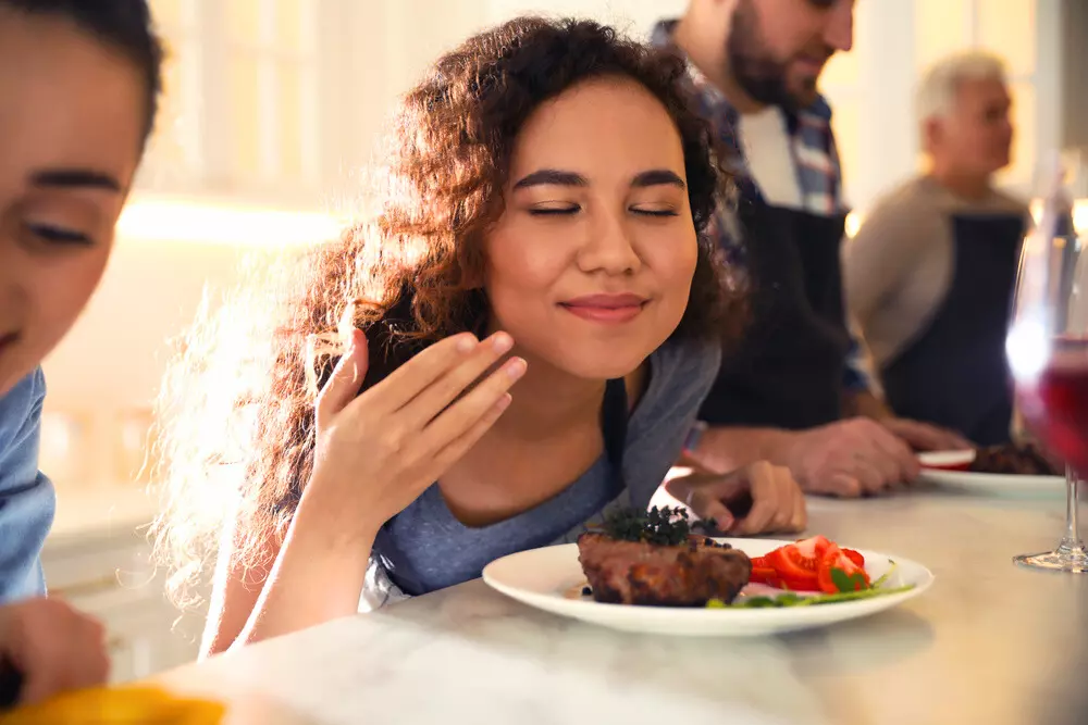 Uma mulher apreciando o aroma de sua refeição com uma bela carne vermelha. Ilustrando a importância da carne vermelha na dieta feminina
