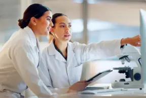 Duas cientistas analisando resultados de pesquisa sobre prebióticos e probióticos em laboratório de microbiologia veterinária, com foco na nutrição animal.