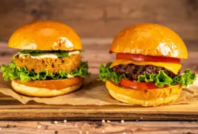 Um hambúrguer de proteína de origem vegetal feito de soja e ao lado um hambúrguer de proteína animal, feito de carne bovina