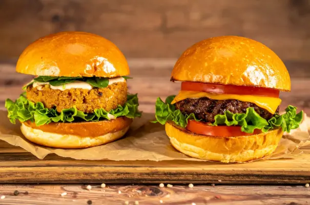 Um hambúrguer de proteína de origem vegetal feito de soja e ao lado um hambúrguer de proteína animal, feito de carne bovina