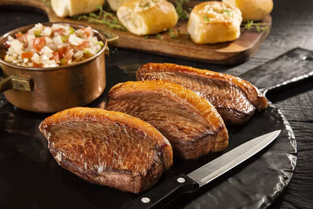 Picanha angus fatiada, carne dos pampas, ao lado de salada e pão, pronta para churrasco, destacando a suculência e sabor tradicional da carne do sul do Brasil.