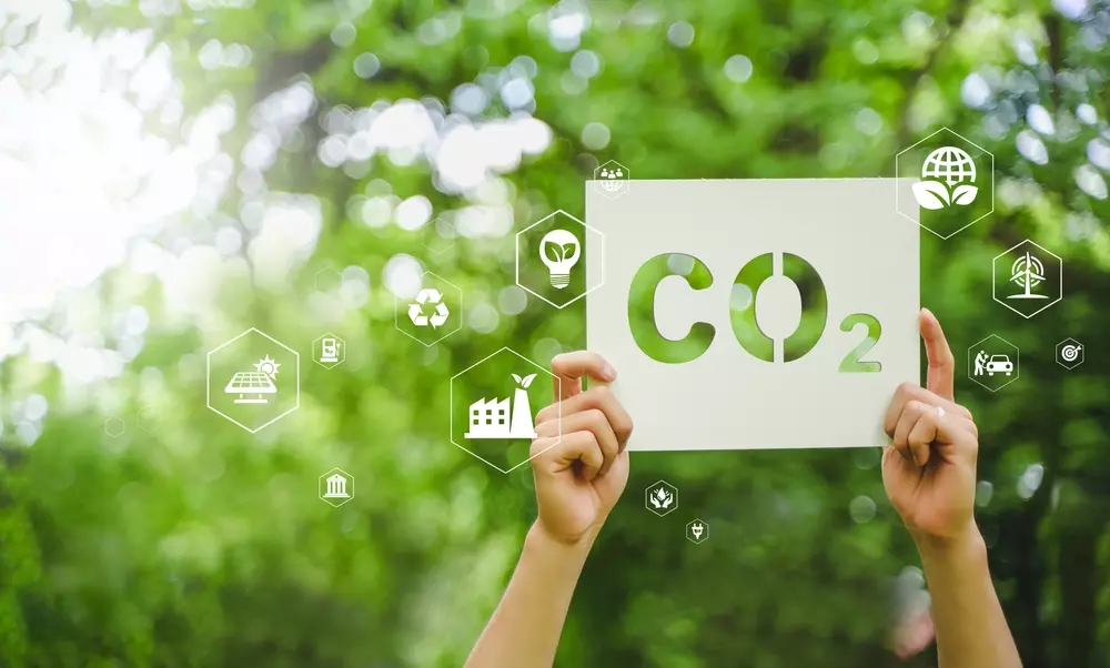 A poster with the CO2 symbol amid a scene of trees and sustainable energy, promoting awareness about reducing carbon emissions and renewable energy.