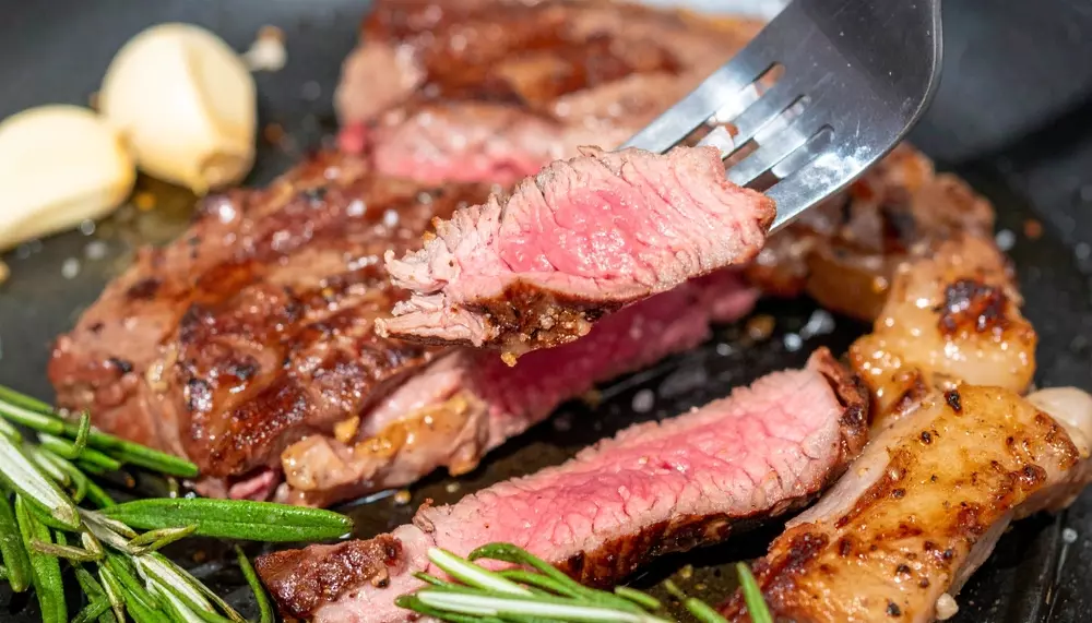 Carne ao ponto suculenta e perfeitamente selada, com crosta dourada e interior rosado, servida com alho e alecrim.