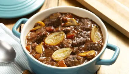 Prato de alcatra cozida com legumes, cebolas e molho, ideal para uma refeição saborosa e nutritiva, servido em uma tigela azul. Perfeito para almoço ou jantar.