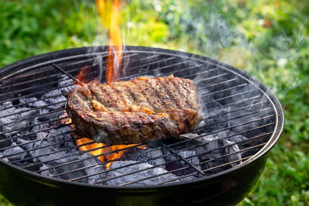 Churrasqueira a carvão com carne grelhada e fumaça, evidenciando a tradição de churrasco ao ar livre.