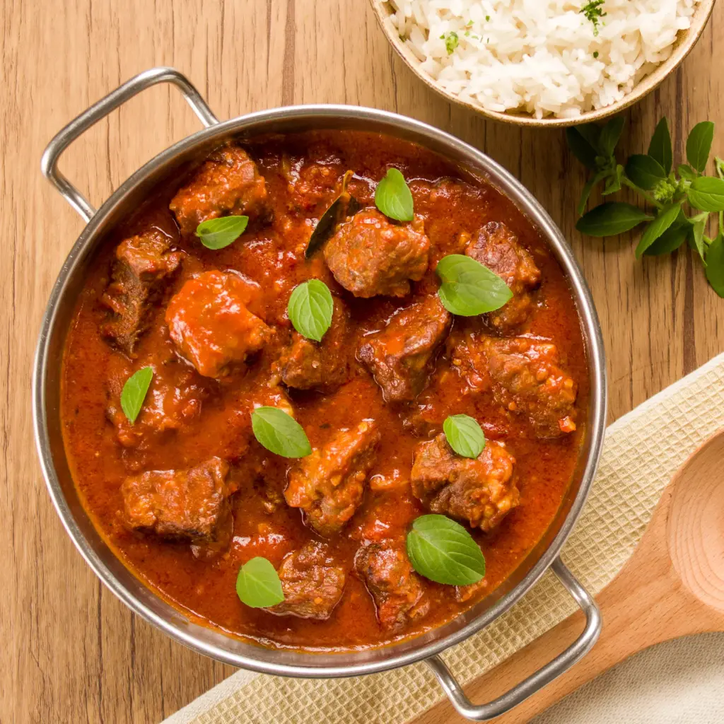 Prato de carne bovina ensopada em molho rico, acompanhado de arroz branco e decorado com folhas de manjericão, ideal para sabores intensos e nutrição.