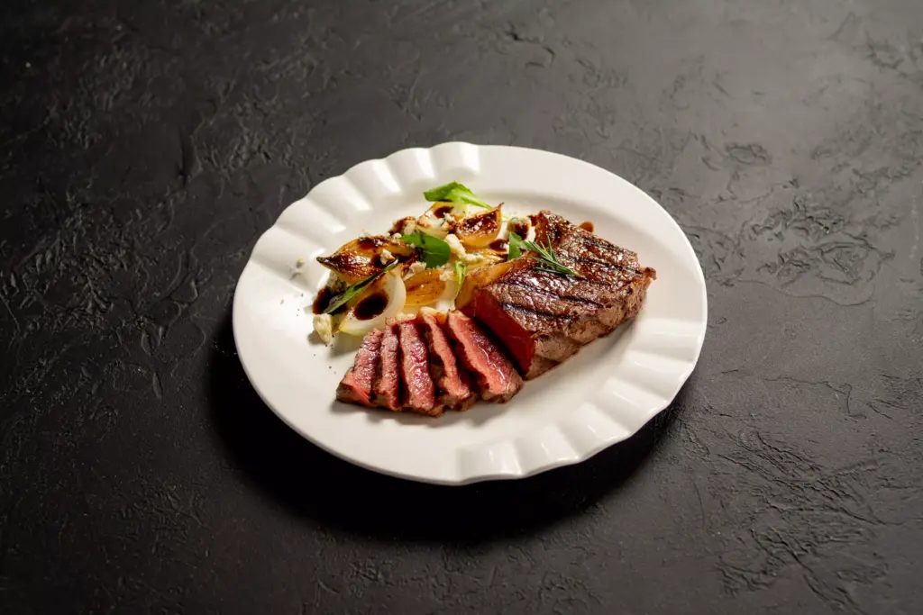 Carne bovina grelhada servida com legumes assados em prato branco, destacando-se na proposta de incluir carne vermelha na rotina alimentar.