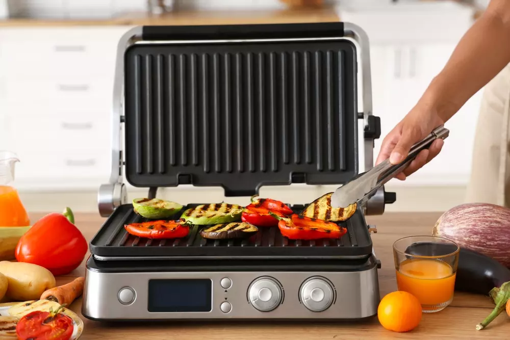 Churrasqueira elétrica com grelhas aquecidas preparando legumes grelhados, foco na alta precisão de cozimento, ideal para churrasqueiras modernas e saudáveis.