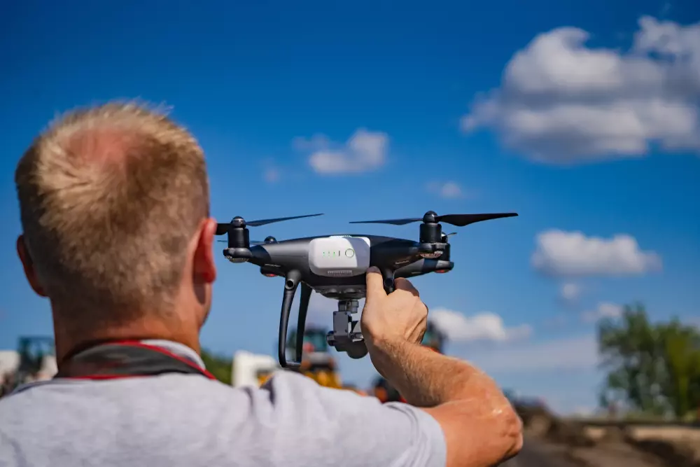 Homem controlando um drone de alta tecnologia ao ar livre sob um céu azul com nuvens, destacando os usos avançados dos drones em diversas áreas.