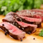 Carne vermelha ao ponto, destacando a presença de mioglobina que dá a cor rosa e vermelha à carne, com tomate e folhas verdes ao fundo.