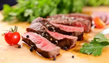 Carne vermelha ao ponto, destacando a presença de mioglobina que dá a cor rosa e vermelha à carne, com tomate e folhas verdes ao fundo.