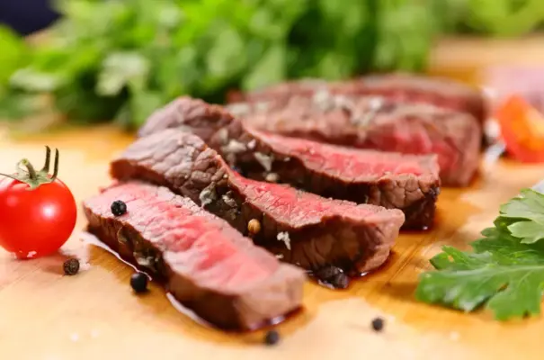 Carne vermelha ao ponto, destacando a presença de mioglobina que dá a cor rosa e vermelha à carne, com tomate e folhas verdes ao fundo.