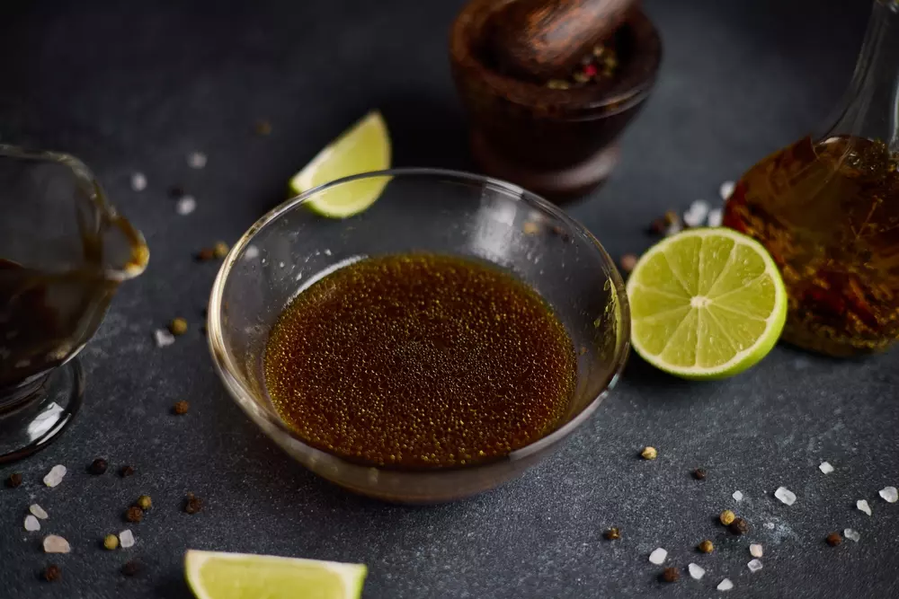A classic acidic marinade in a clear bowl, accompanied by halved lemons, spices and lemon drops on the marinade surface, ideal for enhancing flavors in culinary recipes.