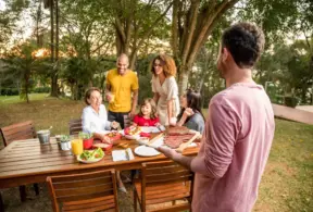 Família aproveitando churrasco de chef ao ar livre com menu variado e ambiente descontraído na natureza.