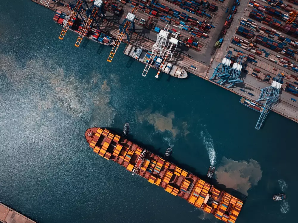 Um porto com movimentação de cargas, destacando contêineres e um navio carregado de caixotes de carnes especiais, simbolizando transporte eficiente e produtos de alta qualidade.