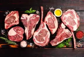 Fiferentes cortes de carne bovina suculenta e bem maturada sobre uma superfície de madeira escura, decorada com temperos, azeite, ervas e sal grosso