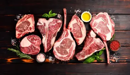 Fiferentes cortes de carne bovina suculenta e bem maturada sobre uma superfície de madeira escura, decorada com temperos, azeite, ervas e sal grosso