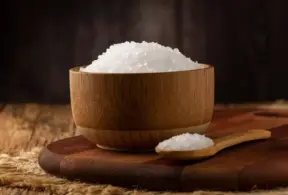 Tigela de madeira sobre uma tábua, com uma colher ao lado, ideal para usos culinários