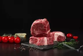 Três pedaços de carne vermelha com tomate cereja, alho e ervas ao redor, destacando a importância dos aminoácidos essenciais na alimentação.