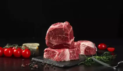 Três pedaços de carne vermelha com tomate cereja, alho e ervas ao redor, destacando a importância dos aminoácidos essenciais na alimentação.