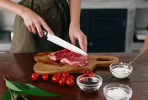 Mulher preparando carne bovina com ingredientes como tomates, sal, pimenta e alho