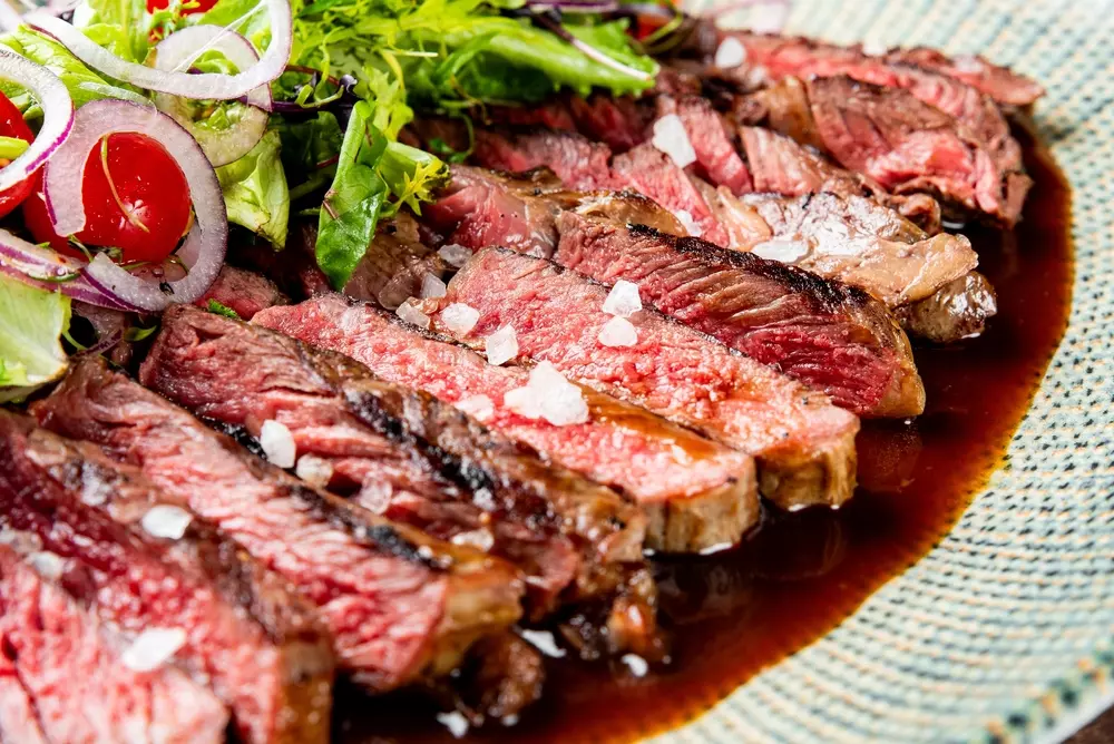 Filé de carne bovina malpassada, servido com salada de folhas verdes, cebola e tomate, destacando o sal em prato apresentando molho escuro