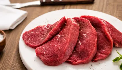 Prato branco com fatias de carne vermelha crua em rodelas grossas, com marcas de gordura e textura, sobre mesa de madeira, Lembrando que ferro heme pode ser encontrado em carne bovina.