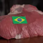 Corte de carne bovina sobre uma mesa de madeira com uma etiqueta da bandeira do Brasil, representando exportação de carne bovina brasileira.