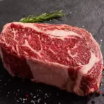 Bife de carne com marmoreio na carne, apresentando textura de gordura entremeada, ideal para churrasco e cortes premium.