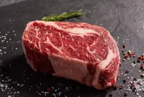 Bife de carne com marmoreio na carne, apresentando textura de gordura entremeada, ideal para churrasco e cortes premium.
