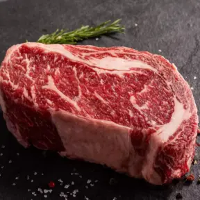 Bife de carne com marmoreio na carne, apresentando textura de gordura entremeada, ideal para churrasco e cortes premium.