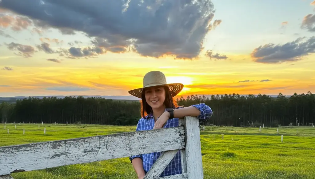 Stephanie Gobato sorridente no campo, com chapéu de palha e camiseta xadrez, representando mulheres na pecuária