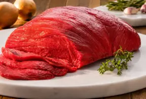Peça de carne bovina vermelha em um prato de pedra com cortes fatiados. Sugerindo a importância do consumo para obter vitaminas como a B12