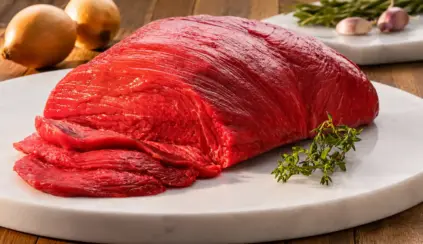 Peça de carne bovina vermelha em um prato de pedra com cortes fatiados. Sugerindo a importância do consumo para obter vitaminas como a B12